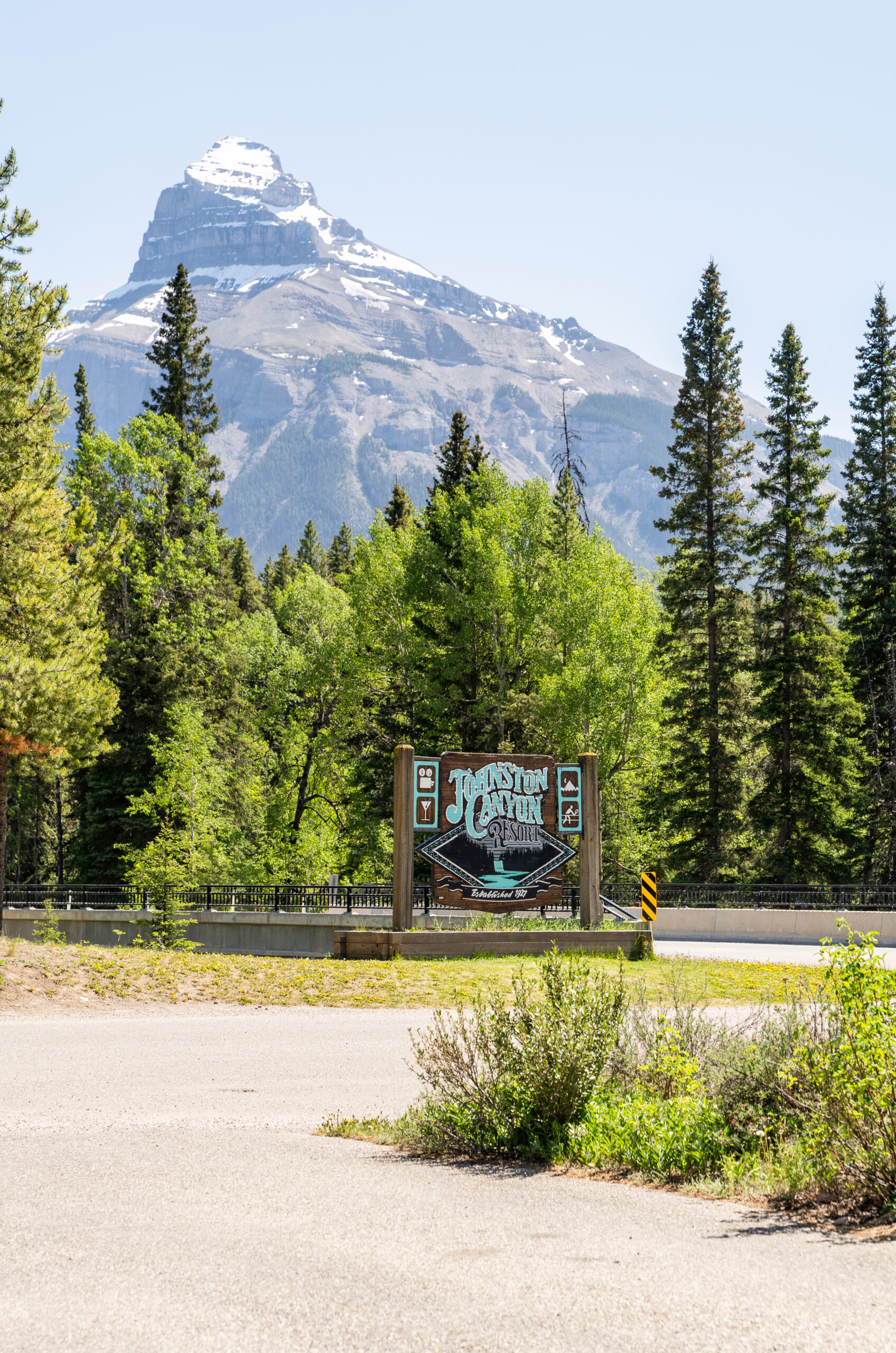 Sign for Johnston Canyon Lodge alongside the road, sunny & green trees.
